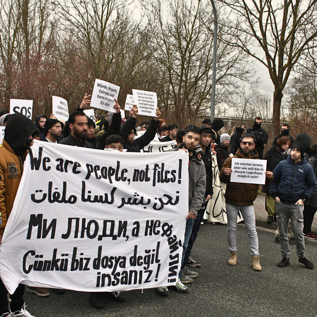 Bewohner demonstrieren in Hermsdorf mit Banner "Wir sind Menschen, keine Akten!" in mehreren Sprachen